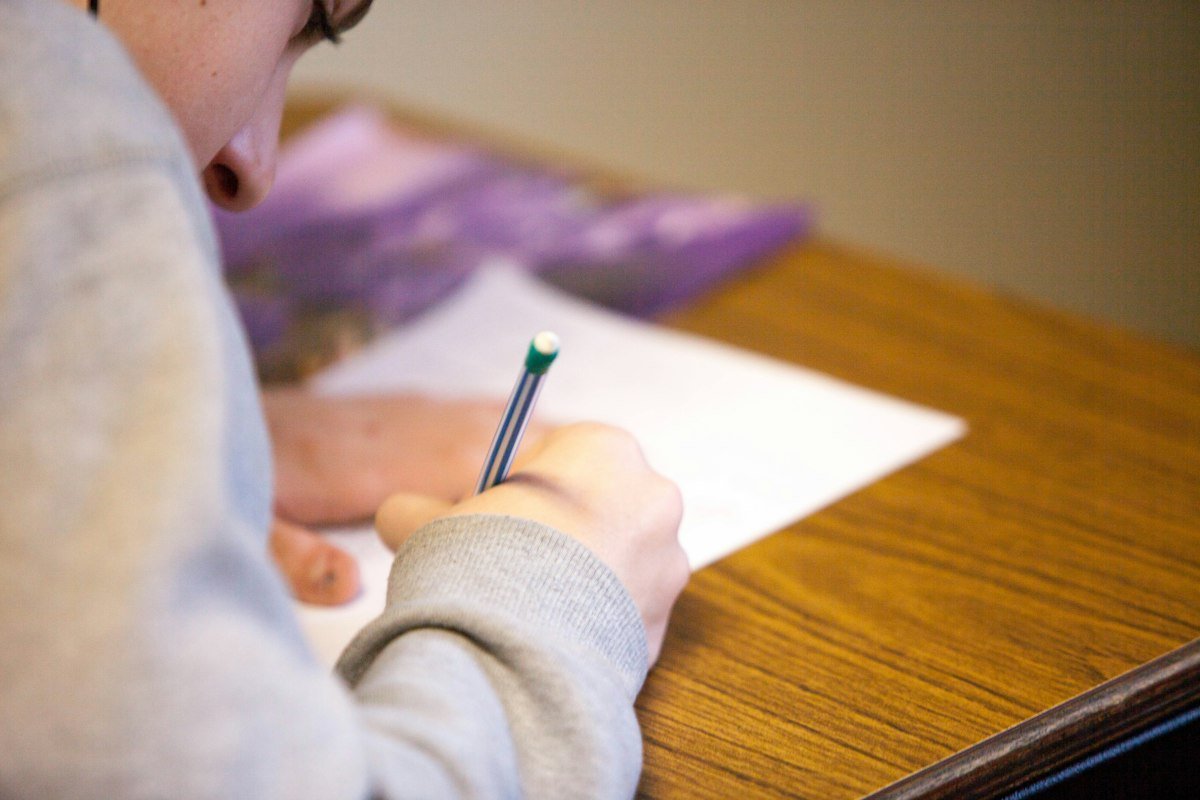 Student writing with a pencil while preparing for IELTS vs PTE vs TOEFL